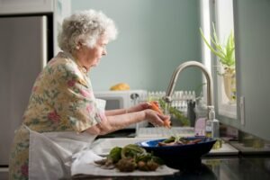 Mujer mayor lava verduras frescas en la cocina